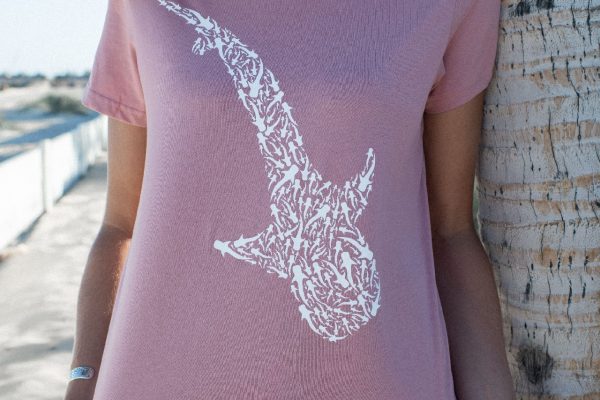 Close-up of a person's back wearing a pink t-shirt with a white whale shark print, standing next to a palm tree.