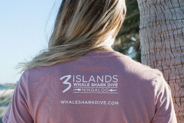 The back of a person wearing a pink shirt with the logo "3 Islands Whale Shark Dive Ningaloo" and the website "whalesharkdive.com".