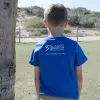 A child in a blue T-shirt with "Three Islands Whale Shark Dive Ningaloo" printed on the back, standing in front of a tree.