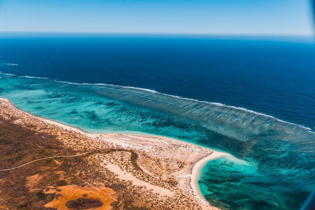 Aerial view of a coastal landscape showing a vivid contrast between the turquoise sea, white sandy beach, and arid land.