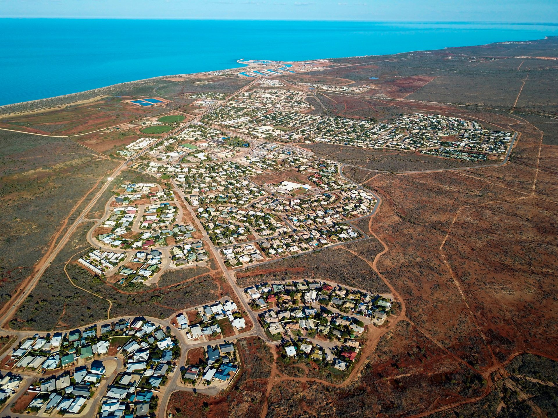 Aerial View of Exmouth WA Showing Coastline, Homes and Red Outback Aerial view of Exmouth, WA showing houses, dry outback terrain, and the blue Indian Ocean in the distance.